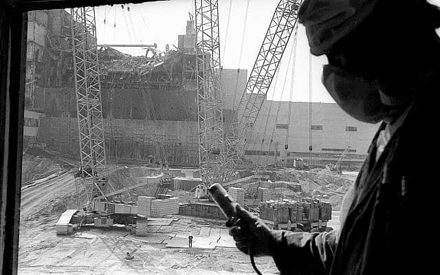 בצילום זה מ-1986, עובד תחנת הכור הגרעינית בצ&#039;רנוביל מחזיק דוזימטר למדידת רמת הקרינה, כשברקע בניית הסרקופג מעל הכור הרביעי ההרוס (צילום: AP\ וולודימיר ריפק)