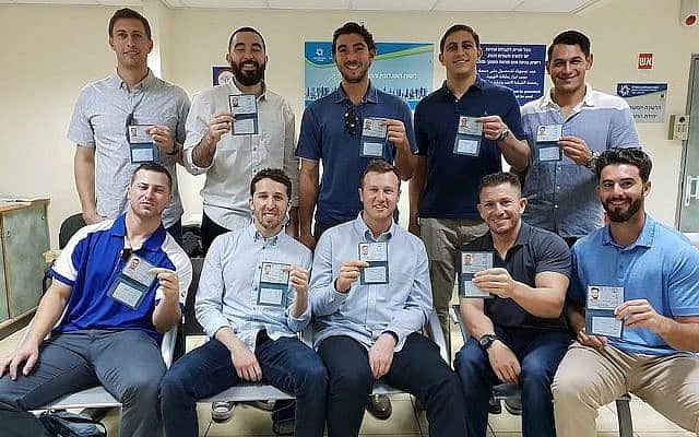 עשרה שחקני בייסבול אמריקאים מראים את תעודות הזהות החדשות שלהם לאחר שקיבלו אזרחות ישראלית, במשרדי רשות האוכלוסייה וההגירה ביפו, ב17 באוקטובר, 2018 (צילום: נבחרת ישראל בבייסבול, דרך JTA)