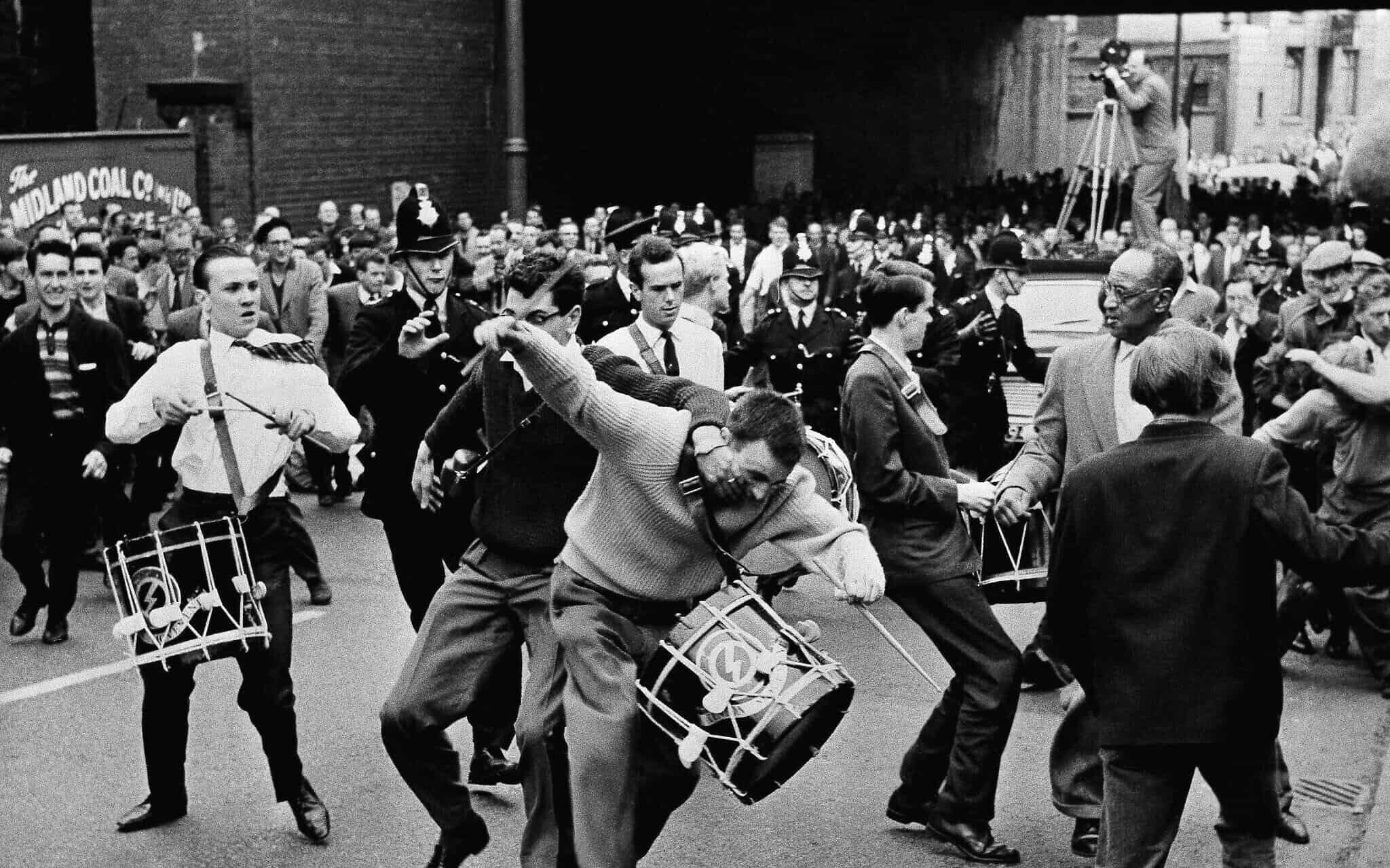 משקיף זועם תוקף את אחד המתופפים של מנהיג הפשיסטים בבריטניה, אוסוולד מוסלי, ראש תנועת האיחוד הימנית הקיצונית, במהלך צעדה במנצ'סטר, אנגליה, ב-29 ביולי 1962. אבנים ועגבניות הושלכו לעבר הצועדים לפני שהם הותקפו פיזית בידי הקהל (צילום: AP)