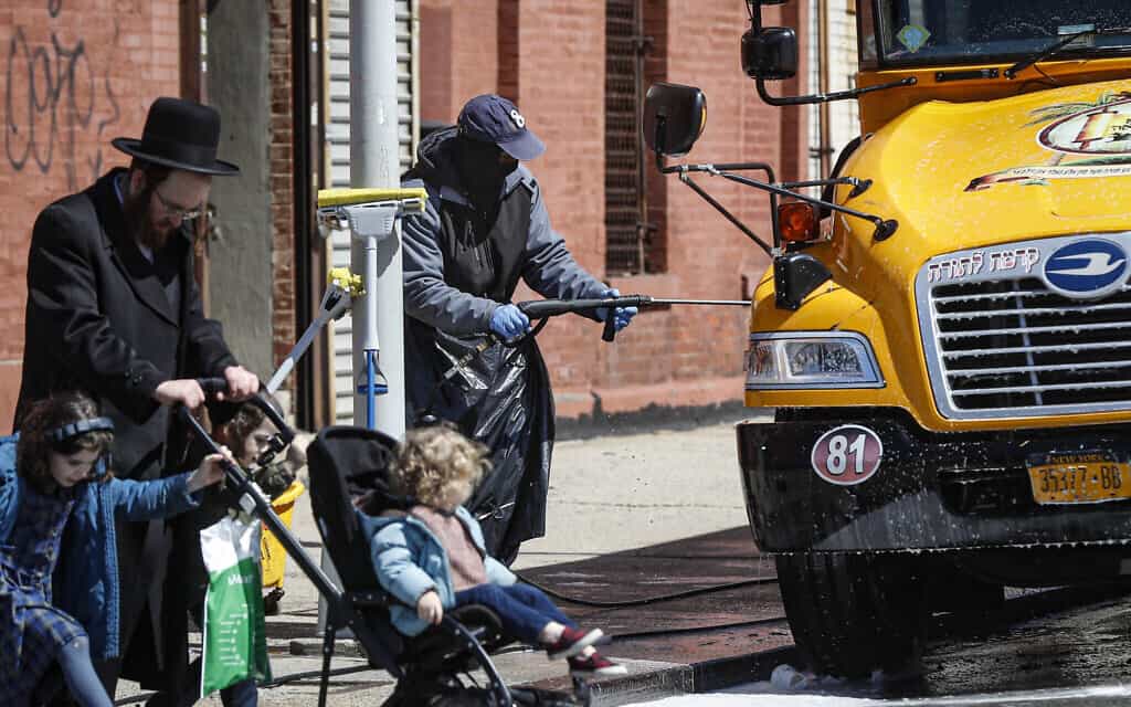 עובד מכוסה בציוד מגן שוטף אוטובוס הסעות של בית ספר המשמש את הקהילה החרדית היהודיות בברוקלין, ניו יורק, 27 במארס, 2020 (צילום: AP\ ג'ון מינצ'ילו)