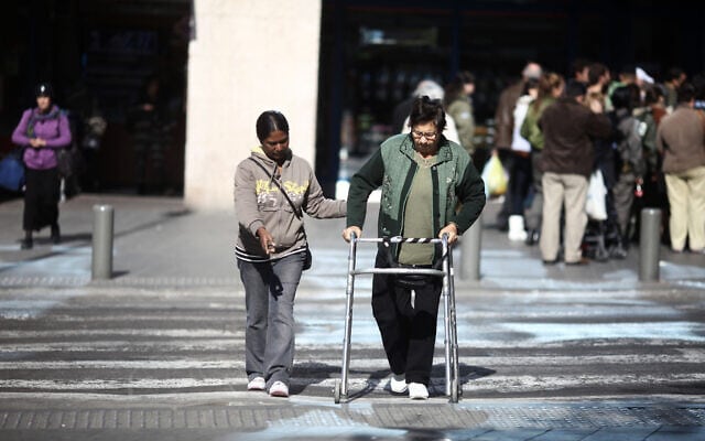 מטפלת פיליפינית מסייעת לקשישה לחצות את הכביש ליד התחנה המרכזית בירושלים. למצולמים אין קשר לנאמר בכתבה (צילום: קובי גדעון/פלאש90)