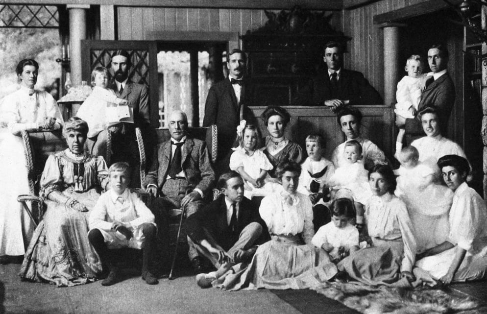 הוריו של גראהם סטוקס (יושבים, משמאל ובמרכז) עם ילדיהם, חתניהם וכלותיהם ונכדיהם באחוזה שלהם בהרי אדירונדאק ב-1907. גראהם עומד כשידיו מונחות על הדלפק, רוז פסטור יושבת על הרצפה, שנייה מימין (צילום: אלבומי סטוקס, כרך 3, אנסון פלפס סטוקס)