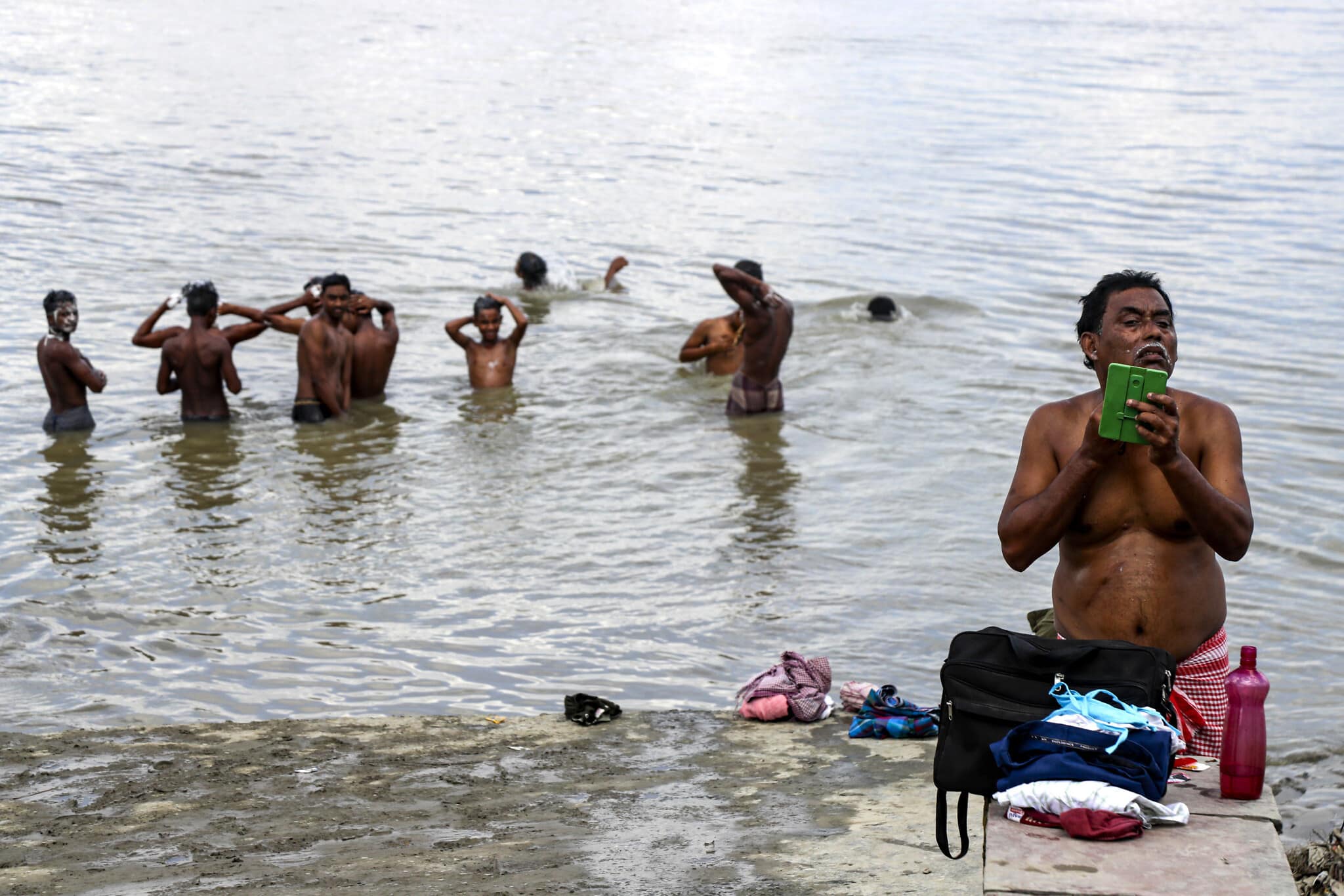 אדם גוזם את זקנו, בעוד שאחרים רוחצים בנהר בקולקטה, ספטמבר 2020 (צילום: AP Photo / Bikas Das)