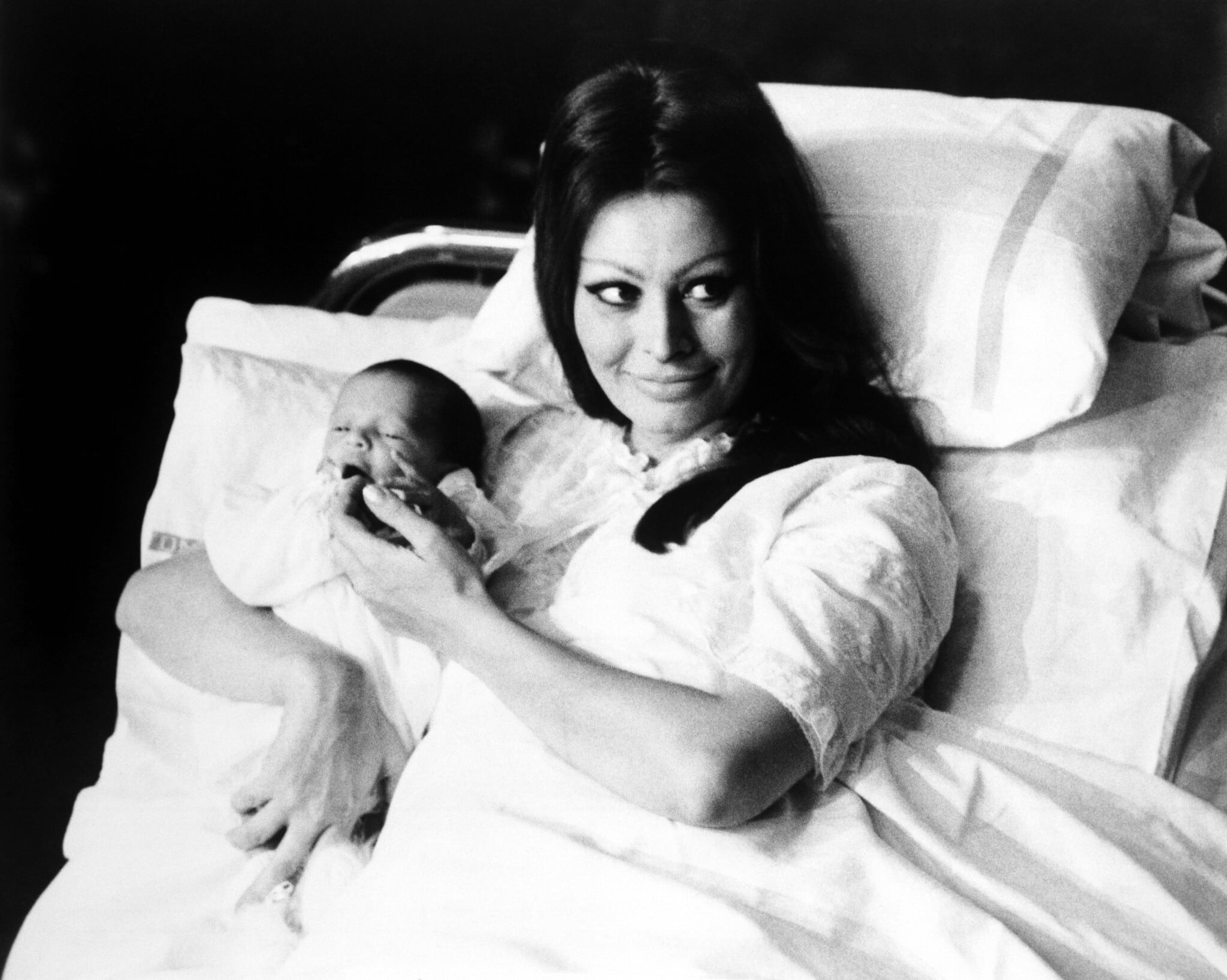 סופיה לורן שוכבת במיטת בית חולים ומחזיקה את בנה קרלו פונטי ג&#039;וניור בזרועותיה, מציגה אותו לעיתונות באולם המרכזי של מרפאת הלידה של בית החולים הממלכתי בז&#039;נבה, שוויץ, ינואר 1969 (צילום: AP)