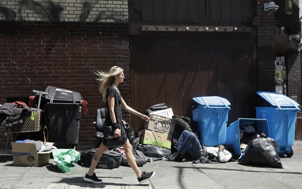 אשה בקליפורניה חולפת על פני הומלס שישן ליד פחי מיחור (צילום: AP Photo/Jeff Chiu)