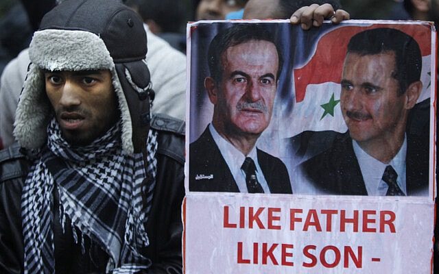 מפגין בבריטניה המוחה נגד המלחמה בסוריה אוחז בשלט עם תמונותיהם של חפז אל-אסד ובנו בשאר, פברואר 2012 (צילום: AP Photo/Lefteris Pitarakis)