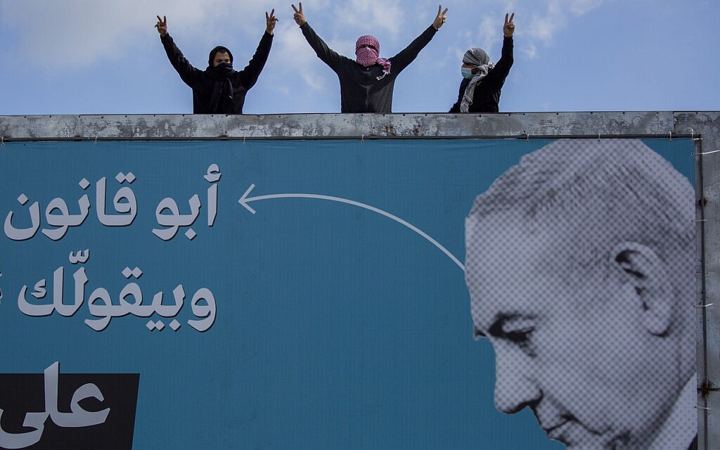 מפגינים ערבים עומדים מעל שלט בחירות של הרשימה המשותפת נגד בנימין נתניהו באום אל פחם, 5 במרץ 2021 (צילום: AP Photo/Ariel Schalit)