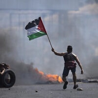 מפגין פלסטיני מנופף בדגל פלסטין בהתנגשויות עם כוחות צה"ל ליד מעבר הגבול חווארה בגדה המערבית, 14 במאי 2021 (צילום: AP Photo/Majdi Mohammed)