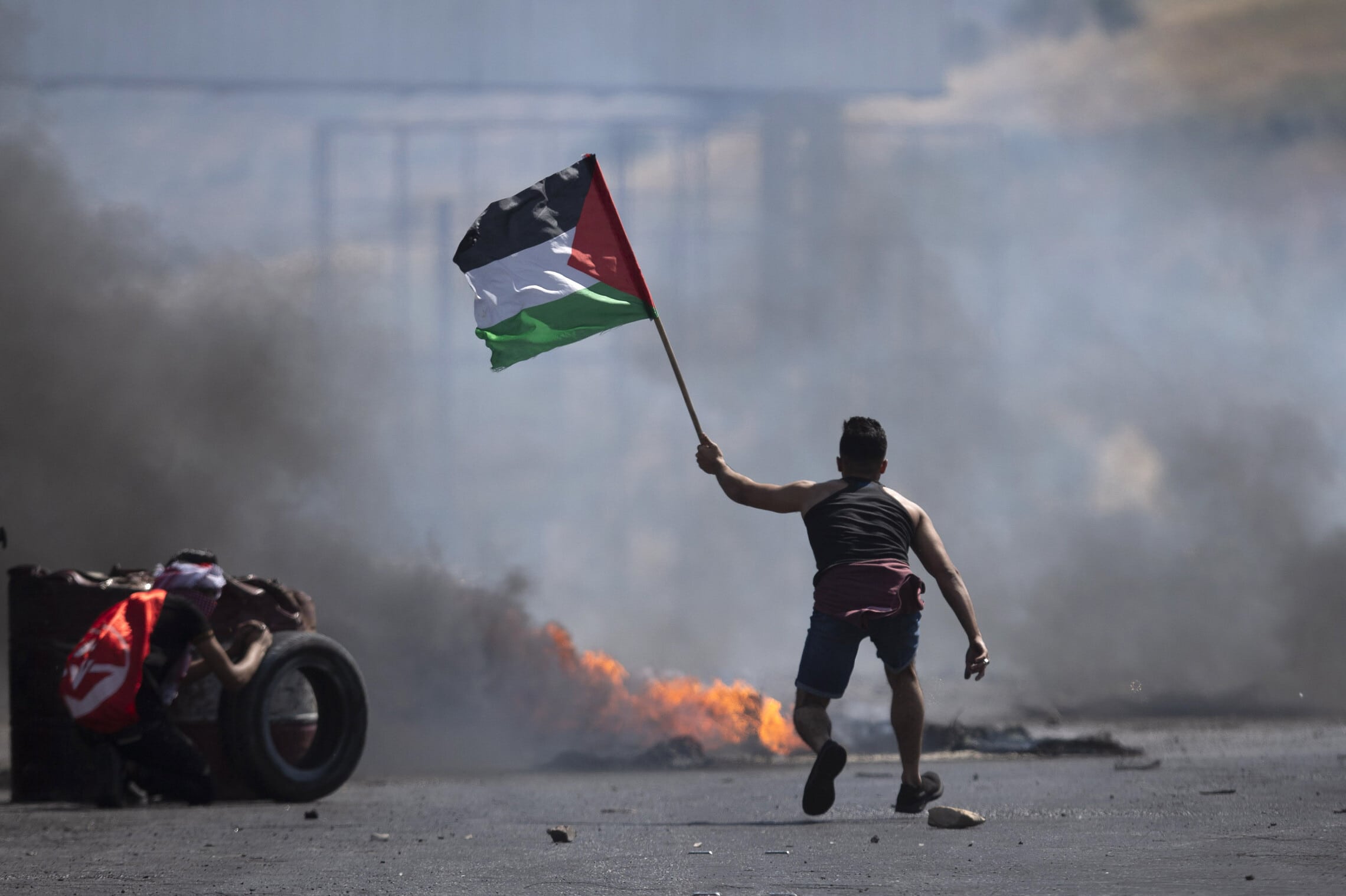 מפגין פלסטיני מנופף בדגל פלסטין בהתנגשויות עם כוחות צה&quot;ל ליד מעבר הגבול חווארה בגדה המערבית, 14 במאי 2021 (צילום: AP Photo/Majdi Mohammed)