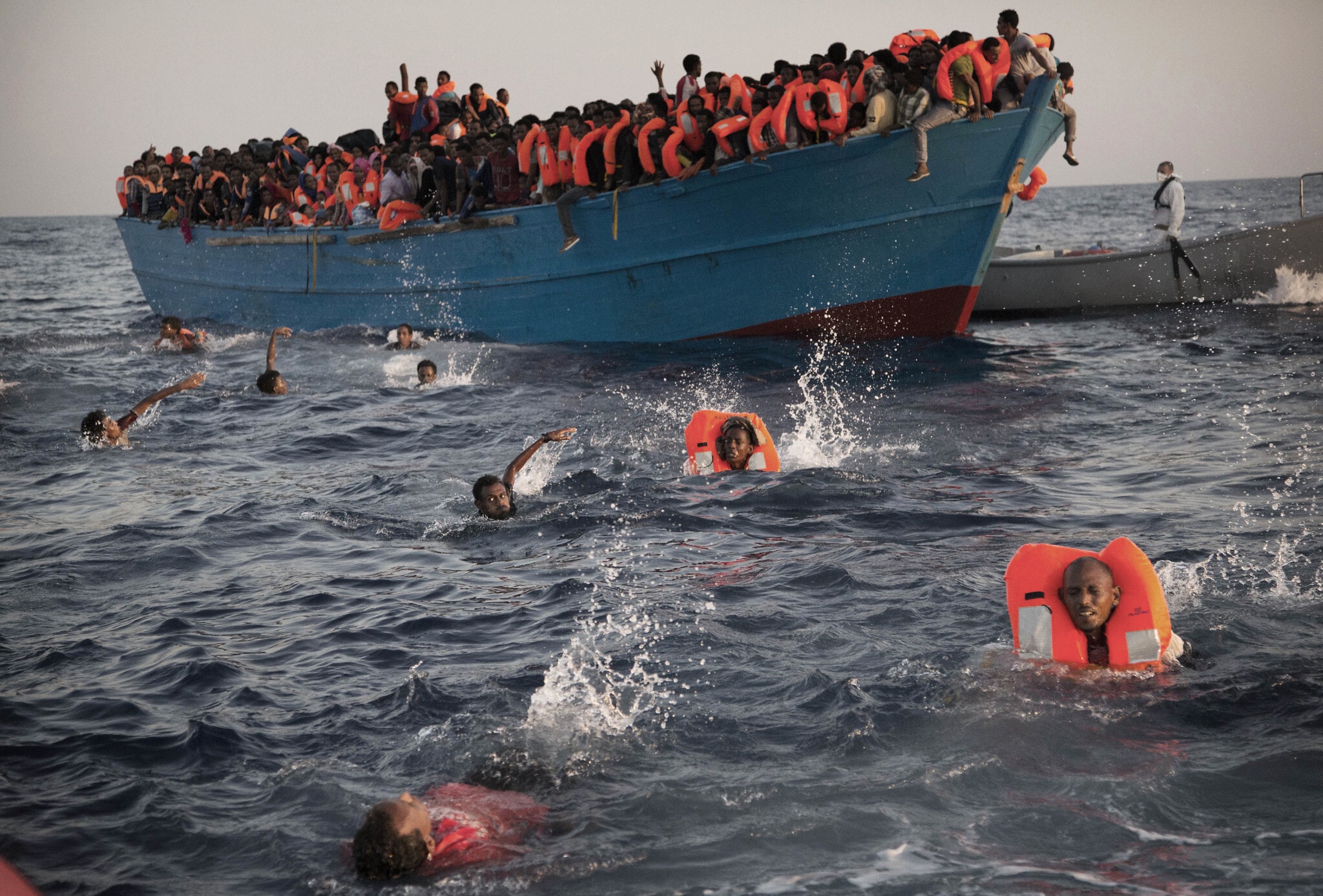 מהגרים, רובם מאריתריאה, קופצים למים מסירת עץ עמוסה במבצע חילוץ של ארגון לא־ממשלתי בים התיכון, כ־20 ק&quot;מ מצפון לסברתה, לוב, 29 באוגוסט 2017 (צילום: AP/Emilio Morenatti)