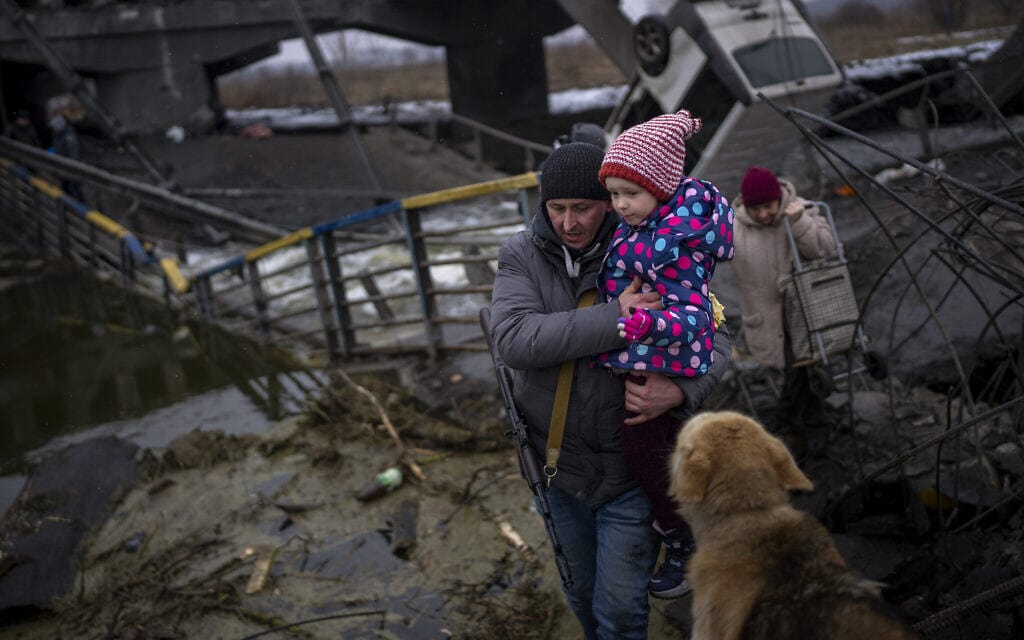 איש כוחות ביטחון אוקראיני מסייע למשפחה לעבור גשר מופצץ בקייב, 2 במרץ 2022 (צילום: AP Photo/Emilio Morenatti)