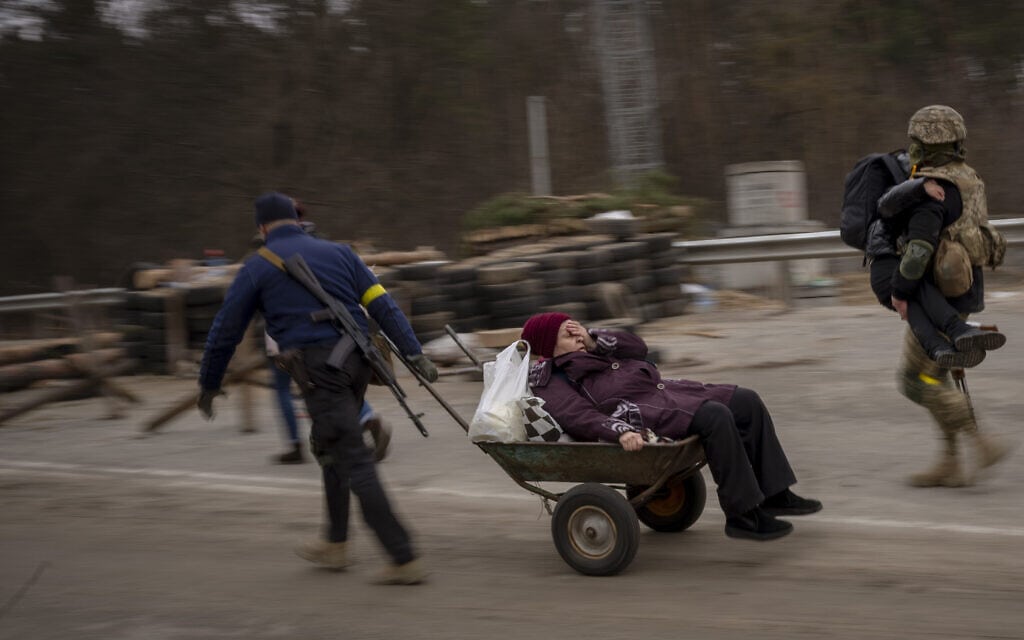חייל ואיש צבא אוקראינים עוזרים למשפחה שנמלטת לחצות את נהר אירפין בפאתי קייב, 5 במרץ 2022 (צילום: AP Photo/Emilio Morenatti)