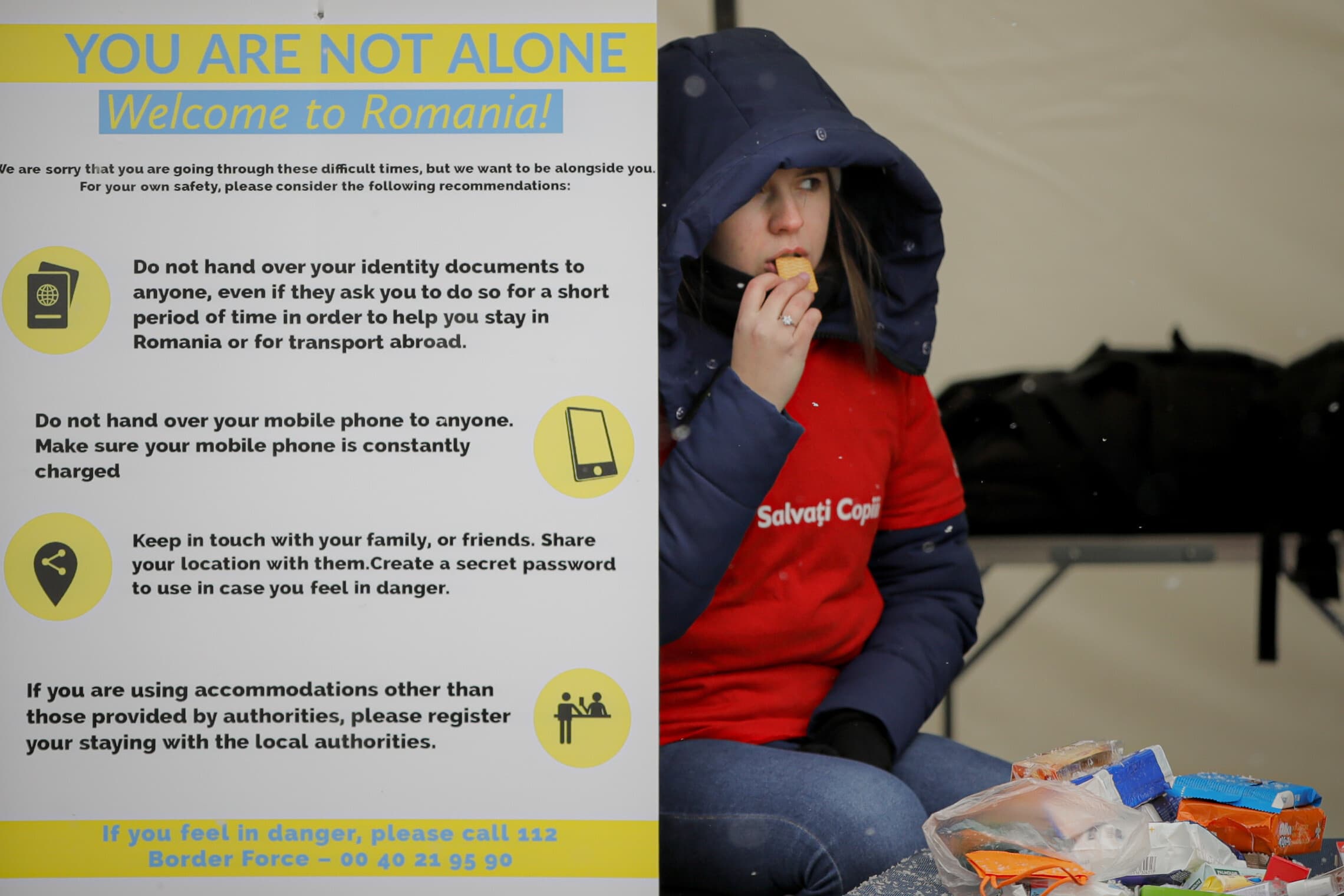מתנדבת בארגון הבינלאומי &quot;להציל את הילדים&quot; יושבת ליד שלט עם הנחיות עבור הפליטים כיצד להישמר, בגבול רומניה-אוקראינה, 7 במרץ 2022 (צילום: AP Photo/Andreea Alexandru)