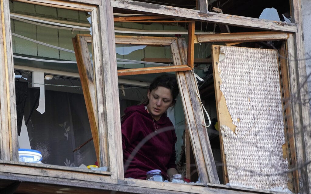 אישה עומדת ליד חלון שבור בדירה בקייב לאחר הפצצה, 14 במרץ 2022 (צילום: AP Photo/Efrem Lukatsky)