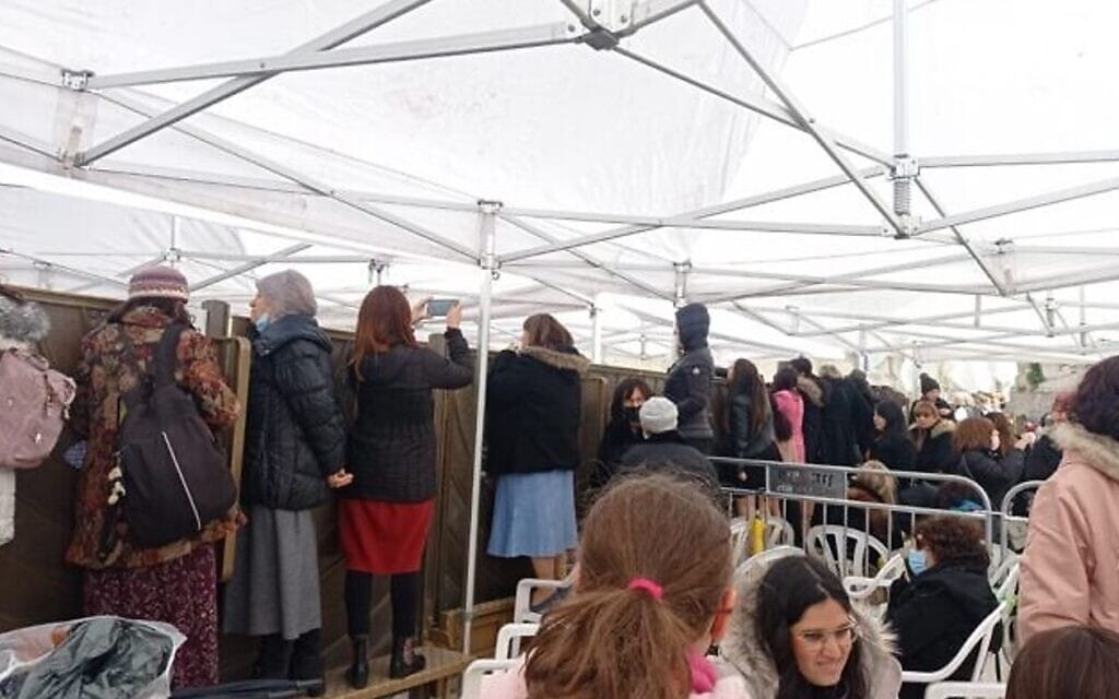 נשים עומדות על ספסלים וכסאות פלסטיק כדי לראות בר מצווה מאחורי מחיצה. (צילום: יוכי רפפורט-זירלר)
