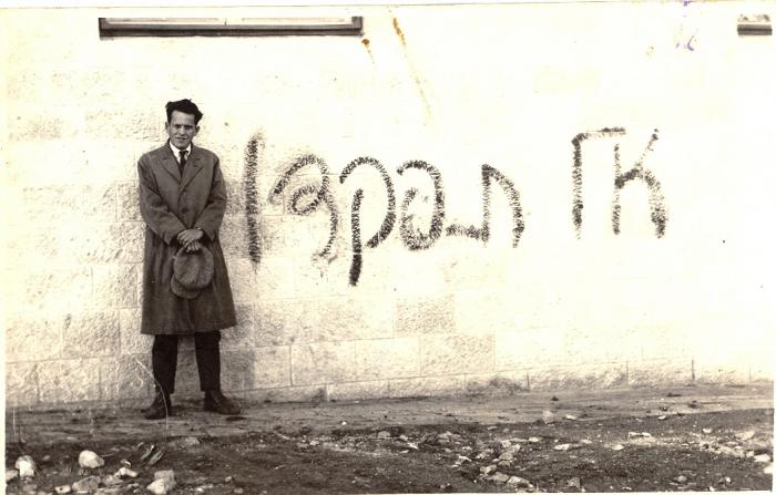 אב&quot;א אחימאיר מצטלם ליד כתובת גרפיטי נגד מפקד האוכלוסין שערך המנדט הבריטי, 1931 (צילום: פיקיוויקי, זכויות ציבוריות)