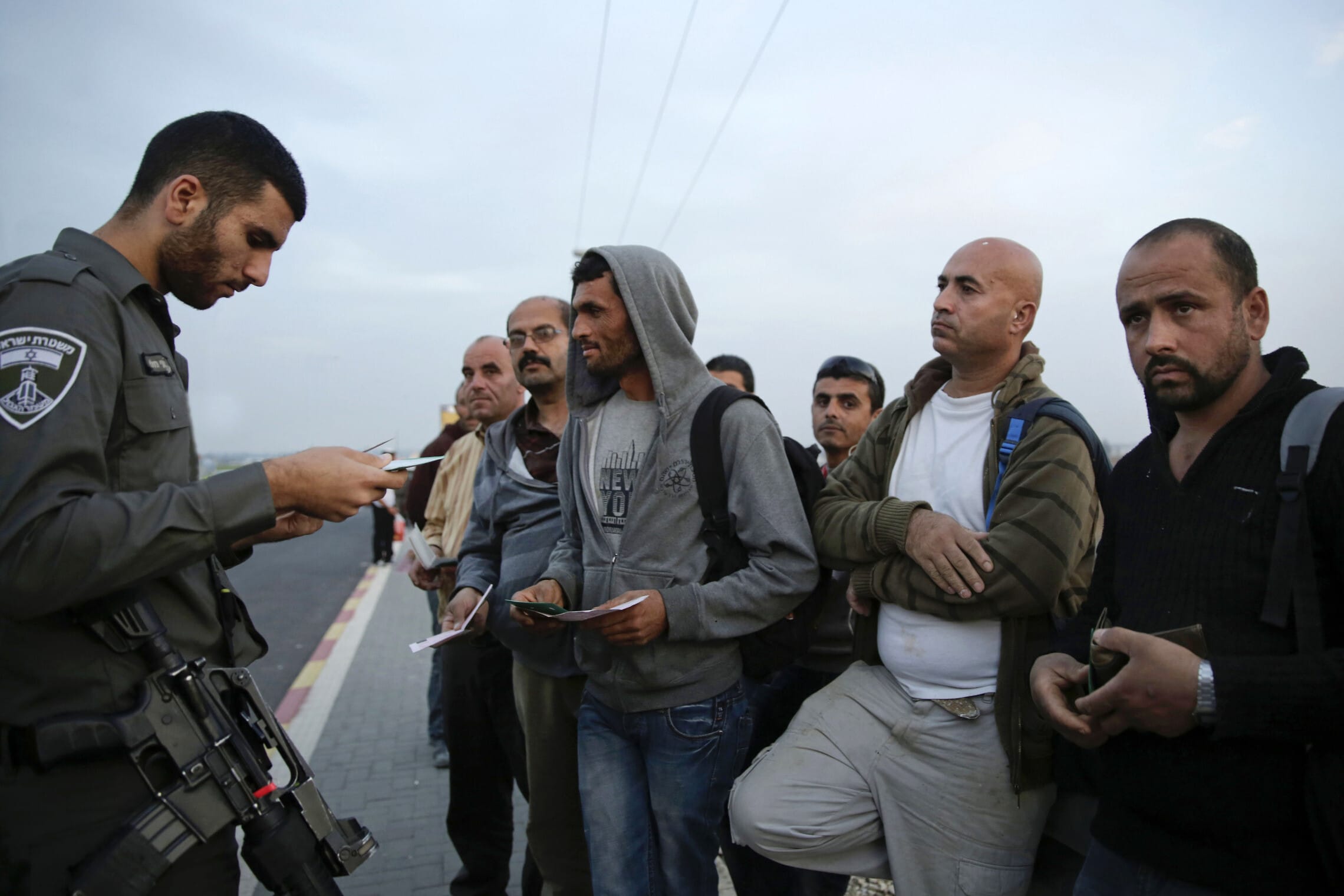 שוטר משמר הגבול בודק את התעודות של עובדים פלסטינים באזור אשקלון,2014 (צילום: AP Photo/Tsafrir Abayov)