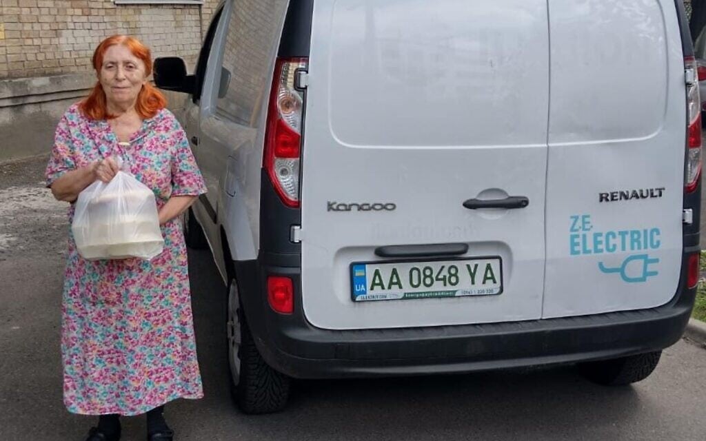 אישה מוציאה חבילת סיוע ממכונית חשמלית של הפדרציות היהודיות של אוקראינה בקייב, 1 באוגוסט 2022 (צילום: באדיבות הפדרציות היהודיות של אוקראינה)