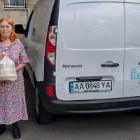 אישה מוציאה חבילת סיוע ממכונית חשמלית של הפדרציות היהודיות של אוקראינה בקייב, 1 באוגוסט 2022 (צילום: באדיבות הפדרציות היהודיות של אוקראינה)