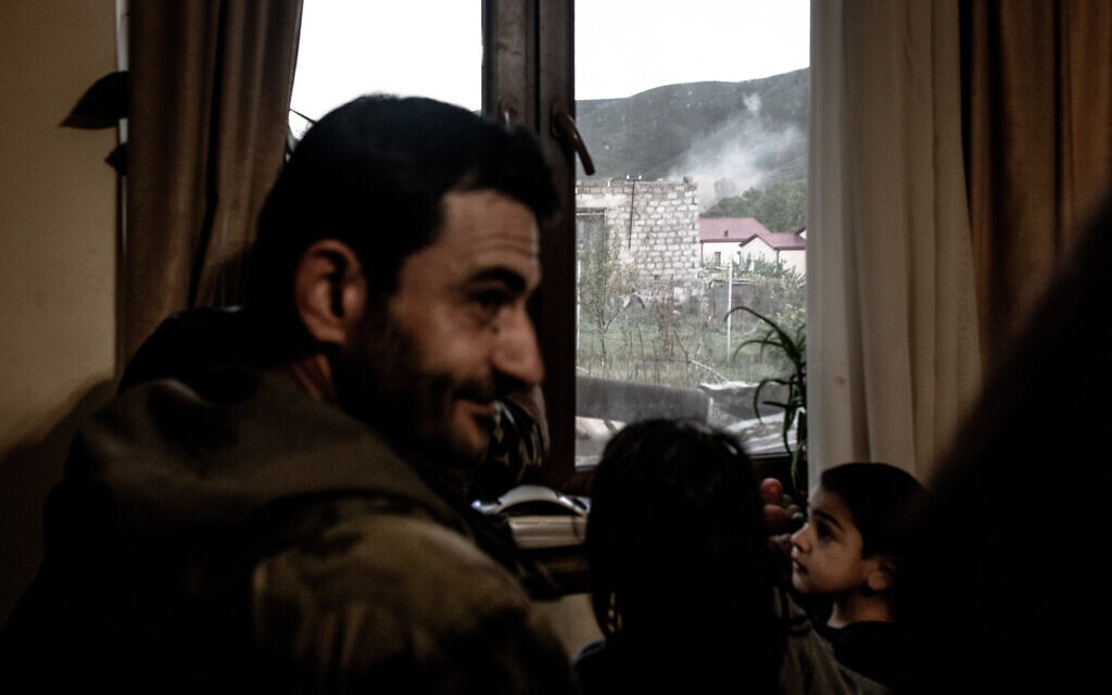 עשן מיתמר בעקבות נפילת פגז בכפר אגהבנו. אנדרניק חוושייאן וילדיו מביטים בנזק מחלון ביתם (צילום: גילעד שדה)