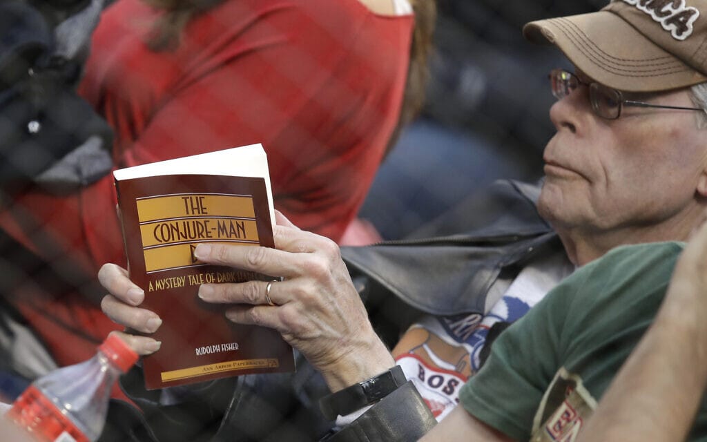 הסופר סטיבן קינג קורא ספר בהמתנה לתחילת משחק בייסבול של הבוסטון רד-סוקס בפנוויי פארק, 1 במאי 2018 (צילום: AP Photo/Charles Krupa)