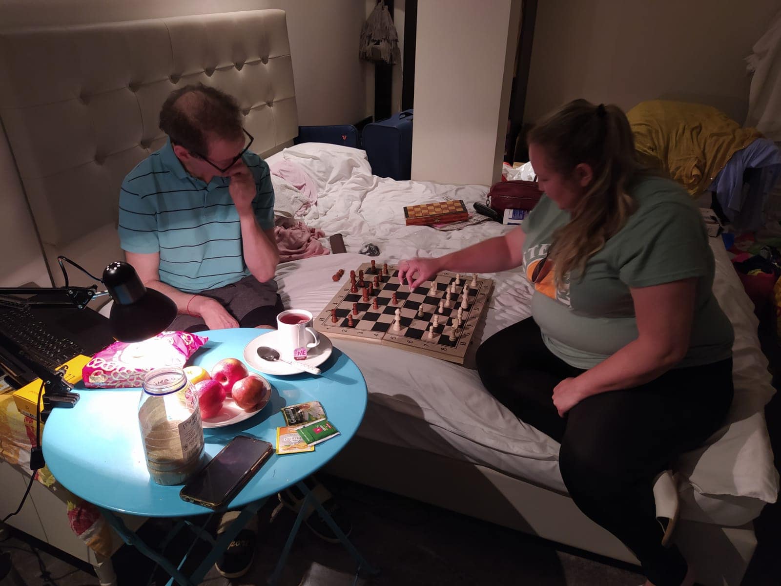 פליטים אוקראינים משחקים שחמט בחדר ללא חלונות בבית מלון בירושלים, יוני 2022. השולחן והמנורה נתרמו על ידי מתנדבים (צילום: באדיבות קטיה צ&#039;כובה)