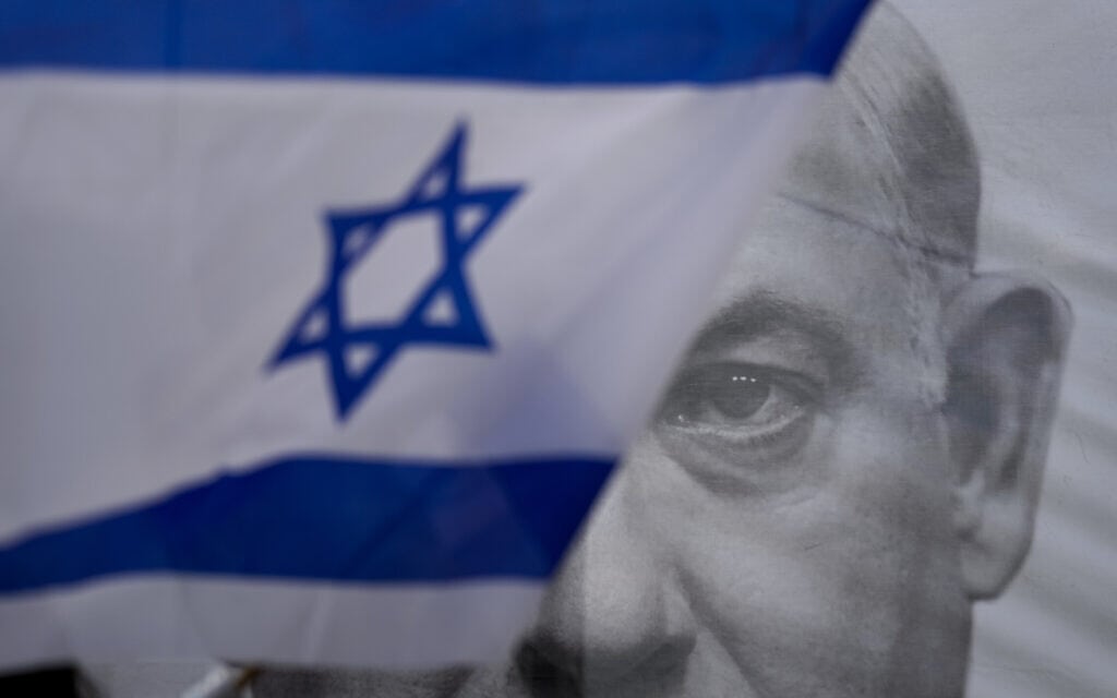 מפגין עם דגל ישראל חולף על פני כרזה עם תמונה של ראש הממשלה בנימין נתניהו, 25 במרץ 2023 (צילום: AP Photo/Ariel Schalit)