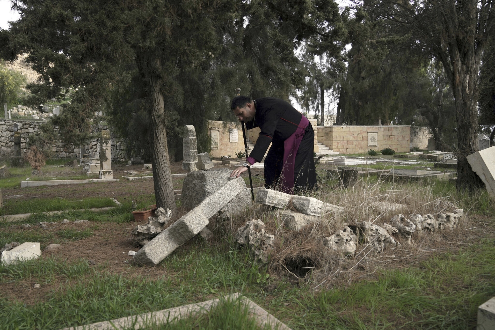 חוסאם נעום, בישוף אנגליקני פלסטיני, נוגע בקבר שהושחת בבית הקברות הפרוטסטנטי ההיסטורי בהר ציון בירושלים, 4 בינואר 2023 (צילום: AP Photo/ Mahmoud Illean)
