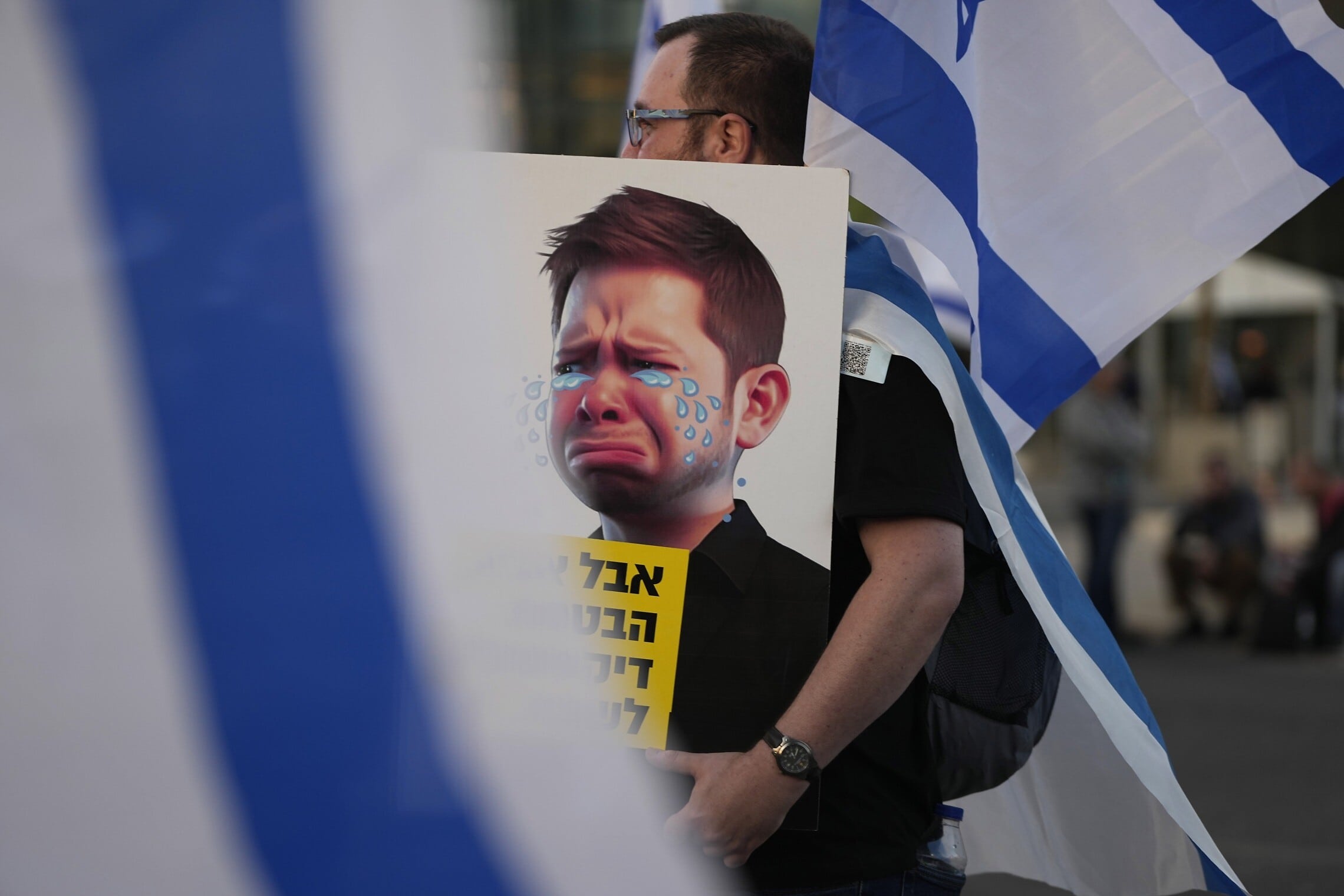 מפגין נגד המהפכה המשפטית מחזיק קריקטורה של יאיר נתניהו בוכה בתל אביב, 1 באפריל 2023 (צילום: AP Photo/Tsafrir Abayov)