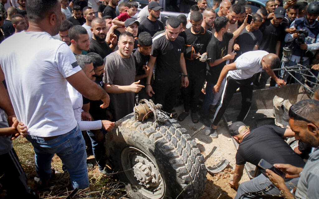 פלסטינים נאספים סביב חלקים של משוריין צה"לי שנפגע ממטען נפץ בג'נין, 19 ביוני 2023 (צילום: Nasser Ishtayeh/Flash90)