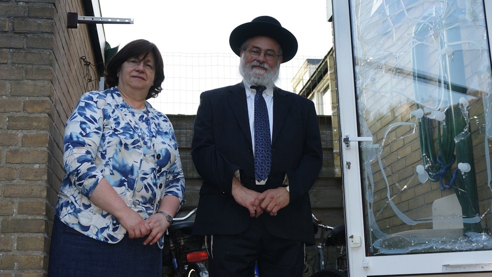 הרב בנימין יעקובס ואשתו בלומה ליד חלון זכוכית שניזוק בתקיפת ביתם, 17 ביולי 2014 (צילום: כנען ליפשיץ / JTA)