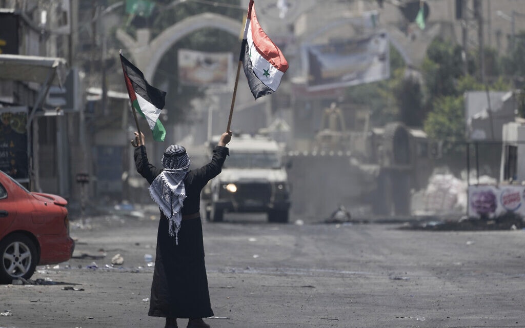 גבר פלסטיני מנופף בדגלים הפלסטיני והסורי מול כוחות צה"ל בג'נין, 4 ביולי 2023 (צילום: AP Photo/Majdi Mohammed)