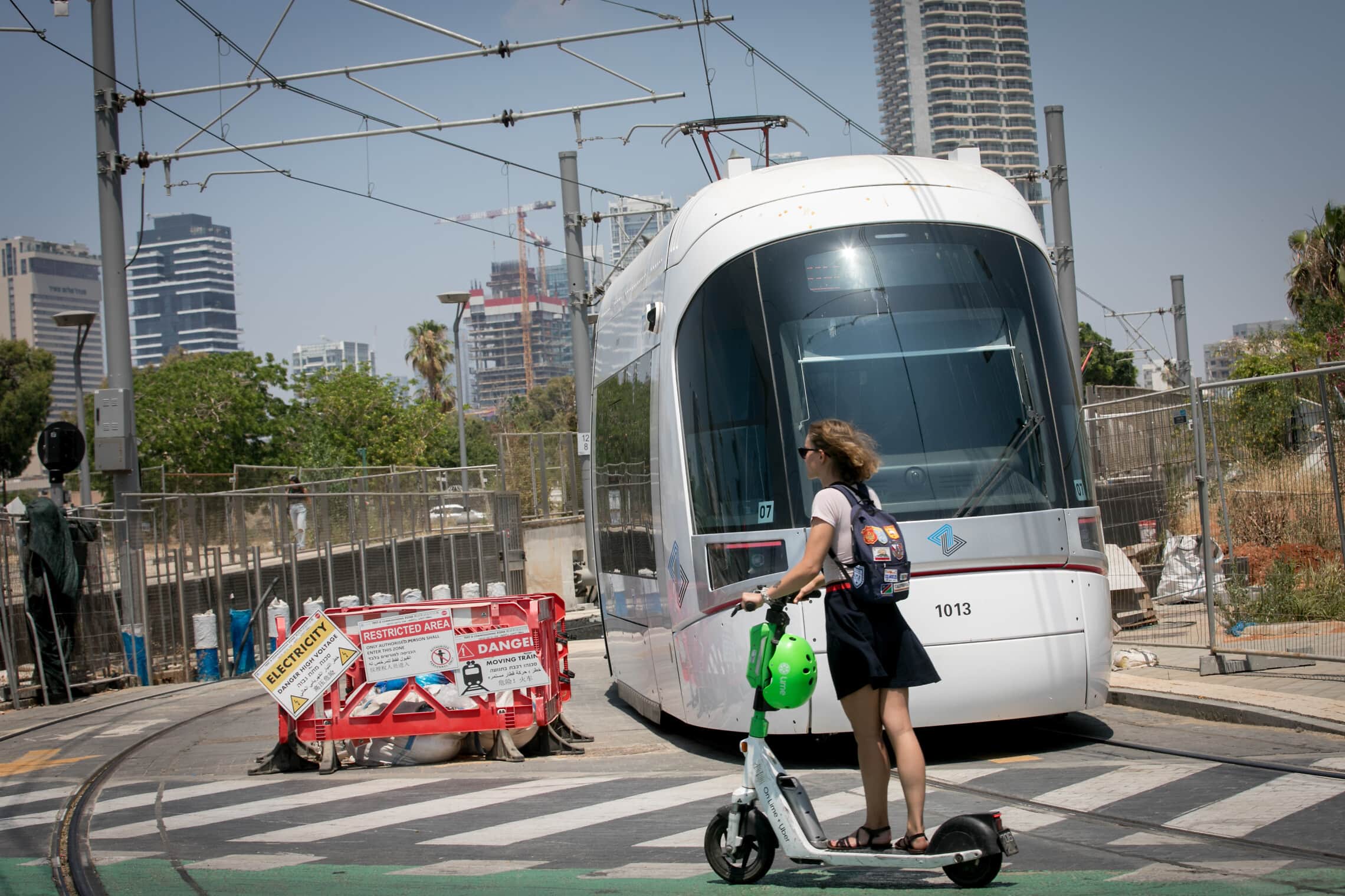 רוכבת קורקינט חולפת על פני הרכבת הקלה בנסיעת מבחן בתל אביב, 6 ביוני 2023 (צילום: מרים אלסטר/פלאש90)