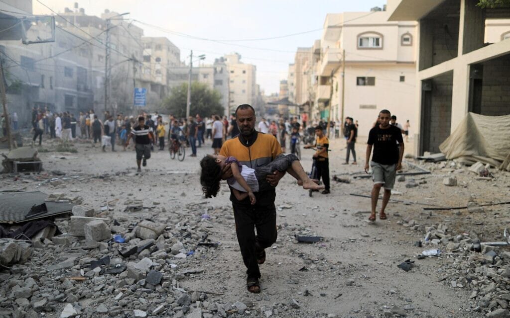 גבר פלסטיני מחזיק ילדה פצועה אחרי תקיפה ישראלית בעזה, 14 באוקטובר 2023 (צילום: YASSER QUDIH / AFP)