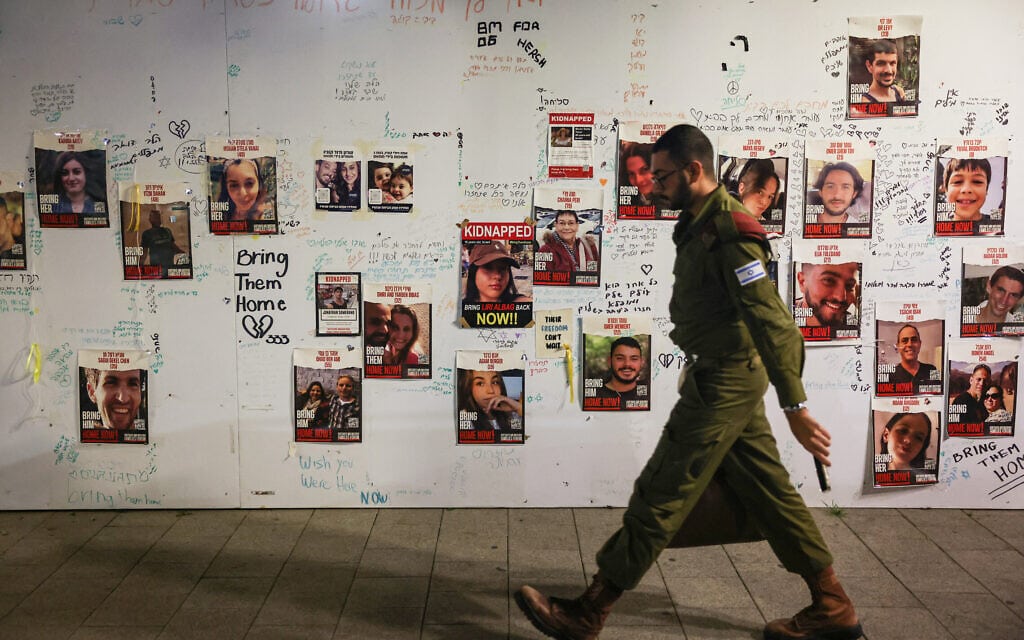חייל צה"ל חולף בתל אביב על פני תמונותיהם של חטופים המוחזקים ברצועת עזה, 22 בנובמבר 2023 (צילום: AHMAD GHARABLI / AFP)