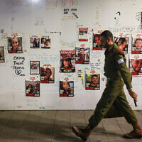 חייל צה"ל חולף בתל אביב על פני תמונותיהם של חטופים המוחזקים ברצועת עזה, 22 בנובמבר 2023 (צילום: AHMAD GHARABLI / AFP)