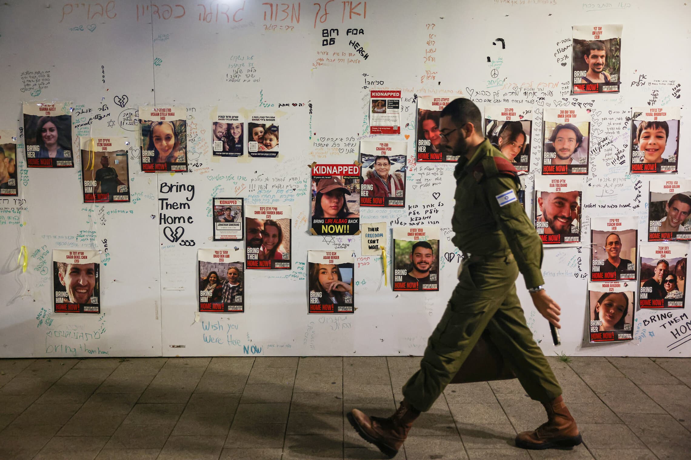 חייל צה&quot;ל חולף בתל אביב על פני תמונותיהם של חטופים המוחזקים ברצועת עזה, 22 בנובמבר 2023 (צילום: AHMAD GHARABLI / AFP)