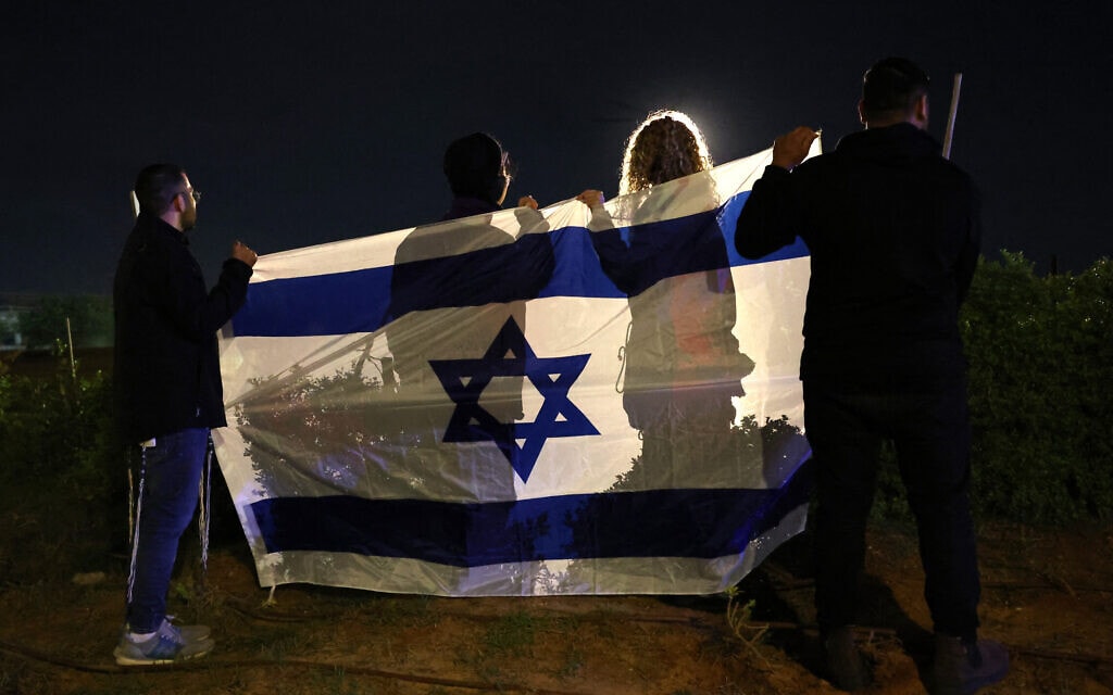 ישראלים עטופים בדגל מנופפים למסוק בו המשוחררים משבי חמאס ליד בית החולים שיבא ברמת גן. 28 בנובמבר 2023 (צילום: JACK GUEZ / AFP)