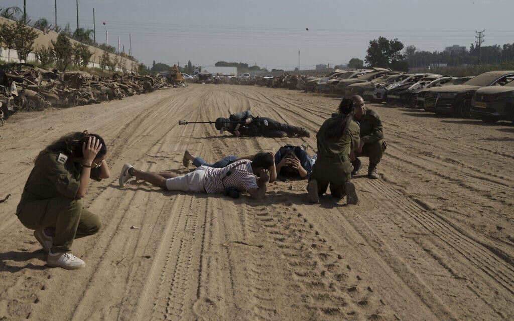 חיילים ועיתונאים נשכבים או יושבים על הקרקע, ליד נתיבות, בשעה שמופעלת אזעקה המתריעה מפני פגיעת טילים ורקטות, 5 בנובמבר 2023 (צילום: AP Photo / Leo Correa)