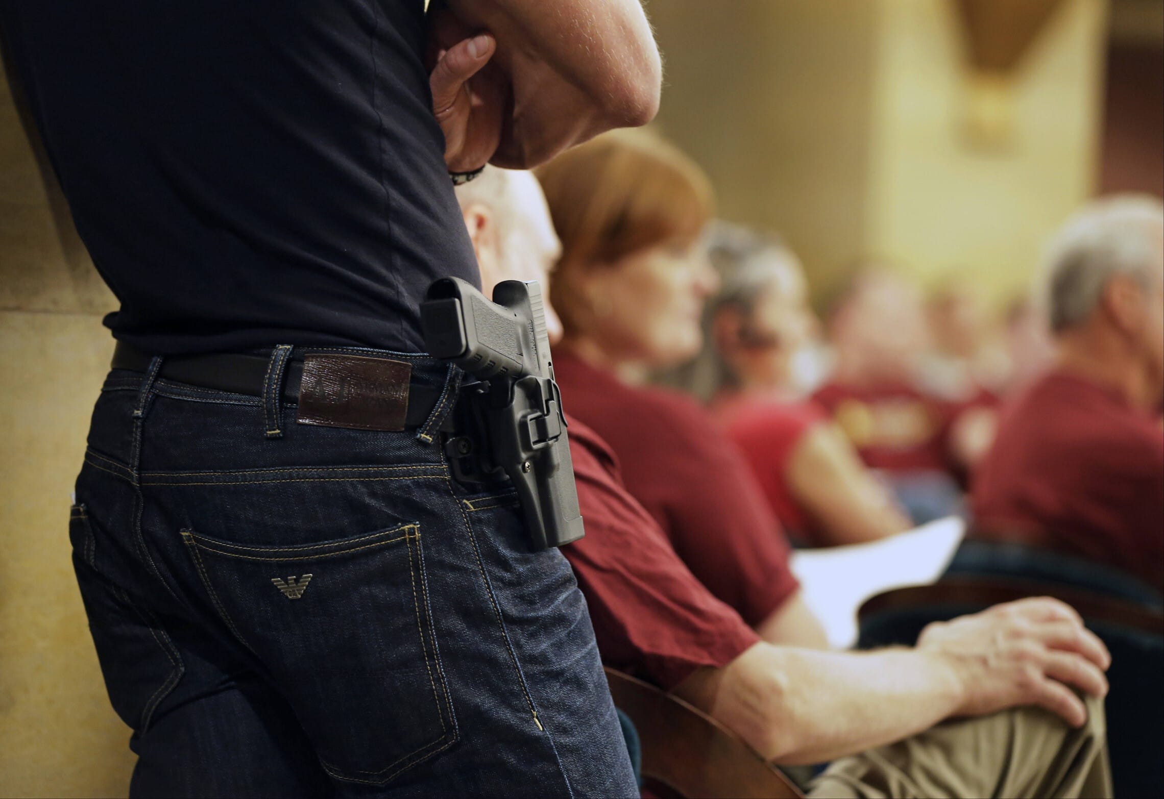 גבר אמריקאי עם אקדח גלוק בחגורתו מאזין לדיון במינסוטה בנושא חוקי נשיאת הנשק במדינה, 26 בנובמבר 2013 (צילום: AP Photo/Jim Mone,File)