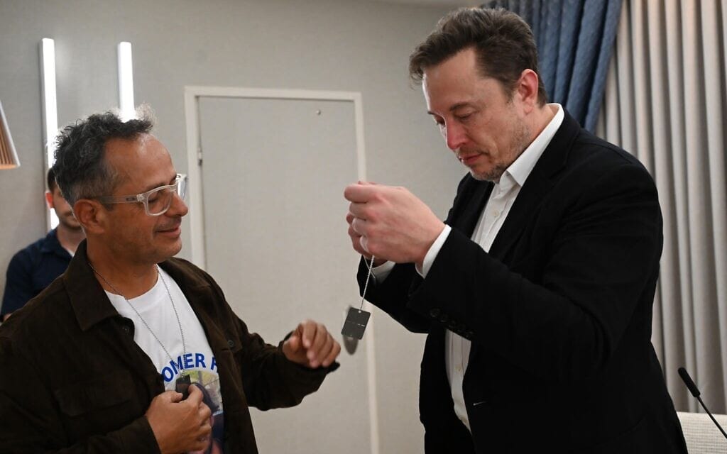 מלכי שם טוב, אביו של עומר שנחטף לעזה מהמסיבה ברעים, עונד לאילון מאסק את דיסקית מטה החטופים, 27 בנובמבר 2023 (צילום: חיים צח/ לע״מ) מלכי שם טוב, אביו של עומר שנחטף לעזה מהמסיבה ברעים, עונד לאילון מאסק את דיסקית מטה החטופים, 27 בנובמבר 2023 (צילום: חיים צח/ לע״מ)