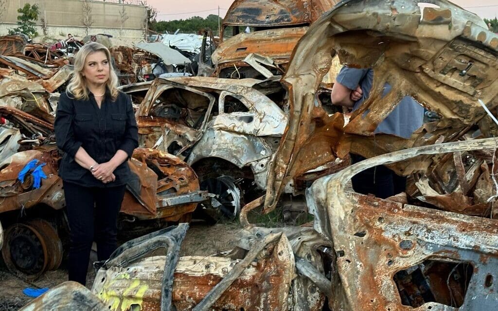 רעיית ראש הממשלה שרה נתניהו לצד מכוניות שנפגעו במתקפה על הדרום ונגררו למגרש גרוטאות. 30 בנובמבר 2023
