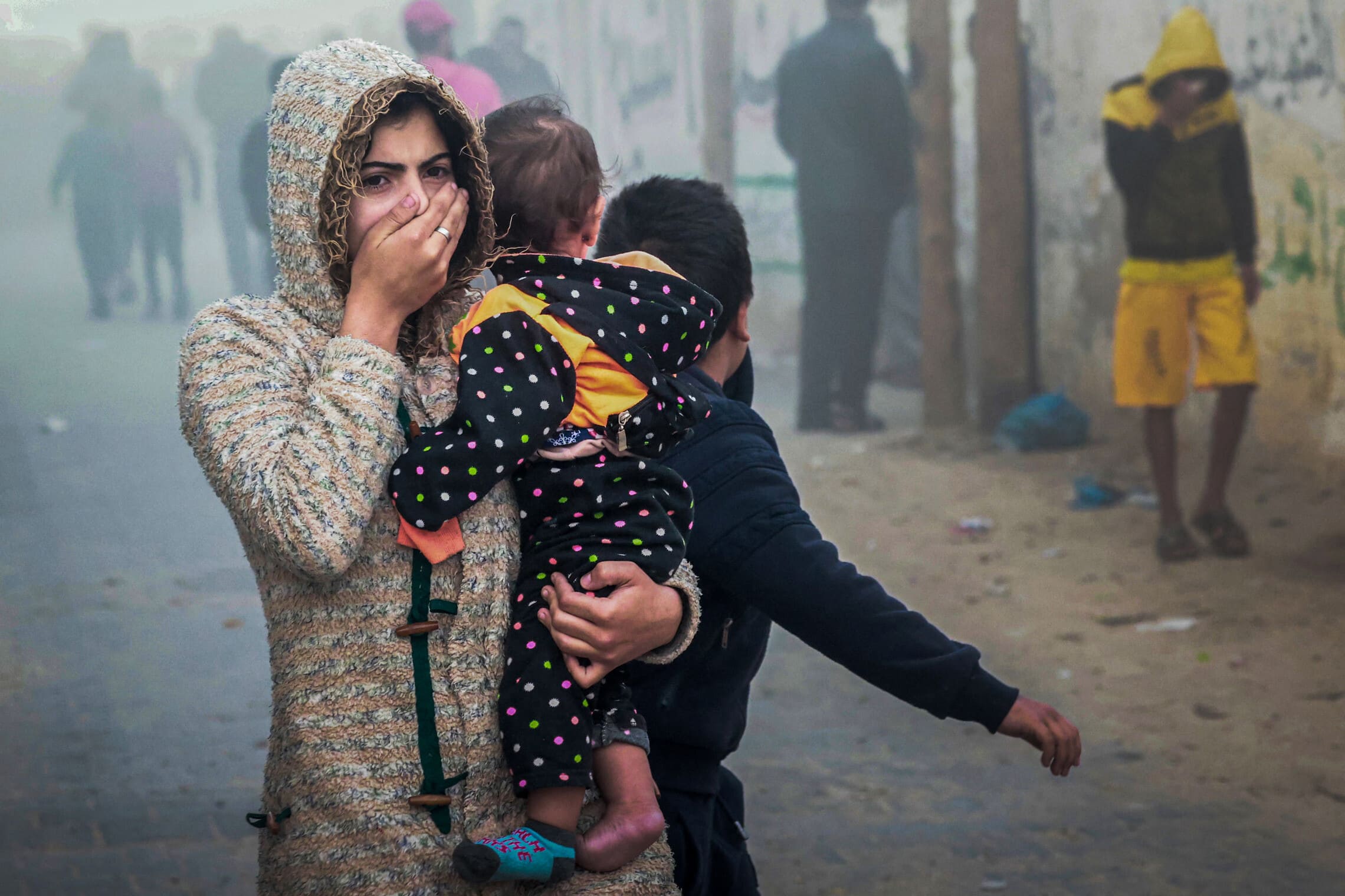 אישה פלסטינית בורחת עם ילד על הידיים מאזור שנפגע בתקיפה ישראלית ברפיח, 23 בנובמבר 2023 (צילום: MOHAMMED ABED / AFP)