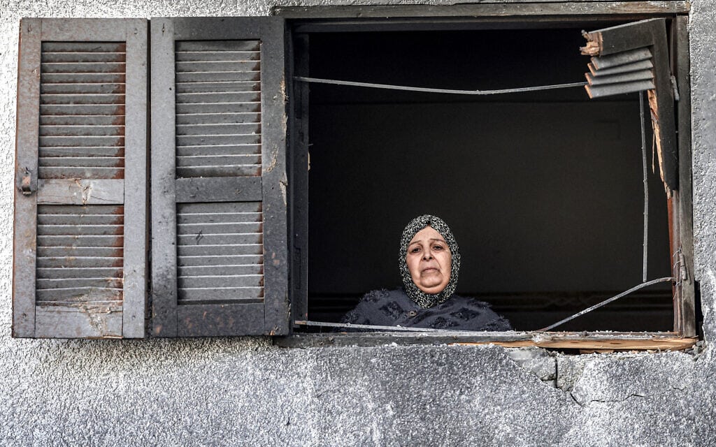 אישה פלסטינית מביטה מחלון הבית השכן בביתה שנפגע בהפצצה ישראלית, 3 בינואר 2024 (צילום: AFP)