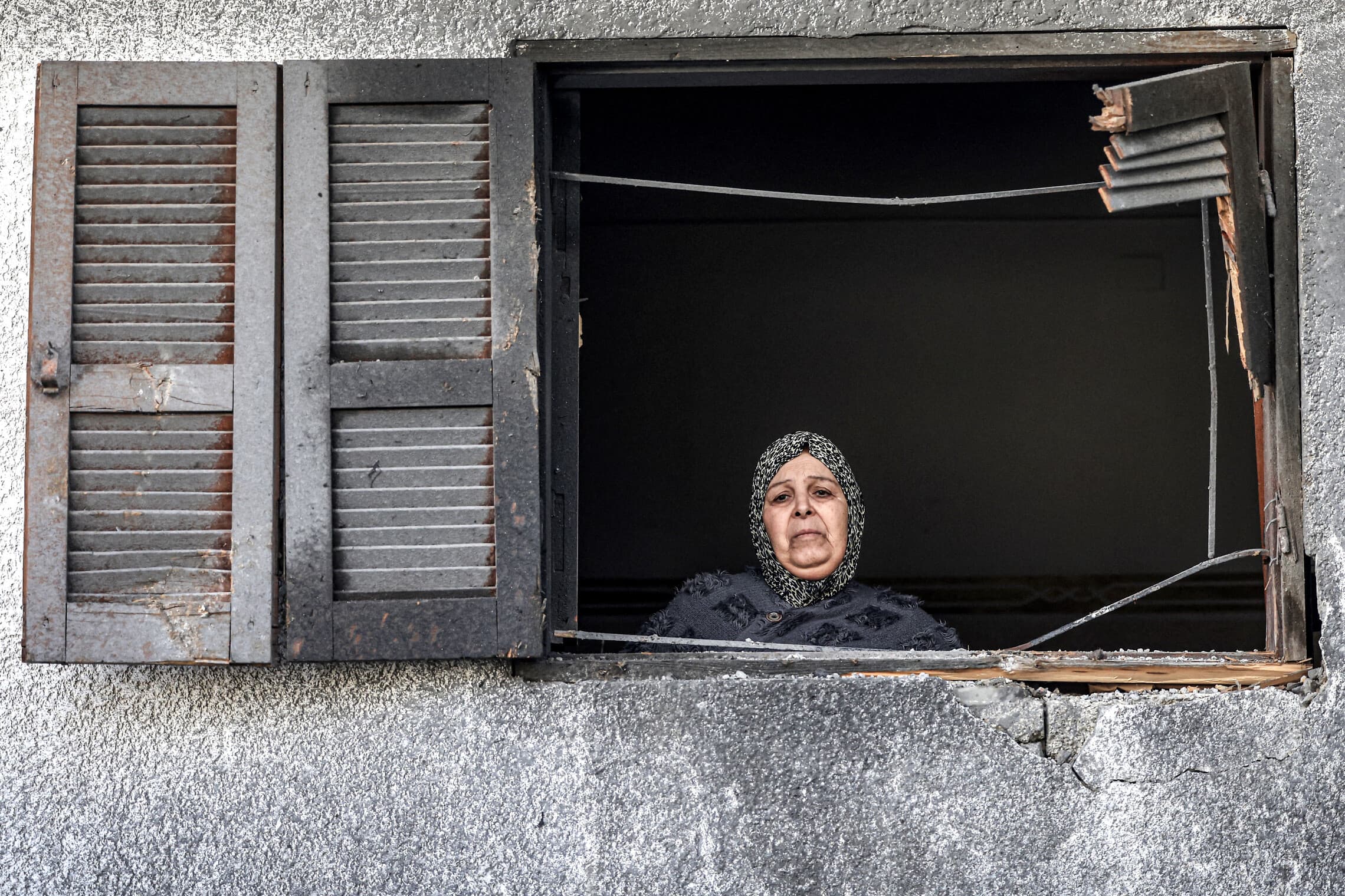 אישה פלסטינית מביטה מחלון הבית השכן בביתה שנפגע בהפצצה ישראלית, 3 בינואר 2024 (צילום: AFP)