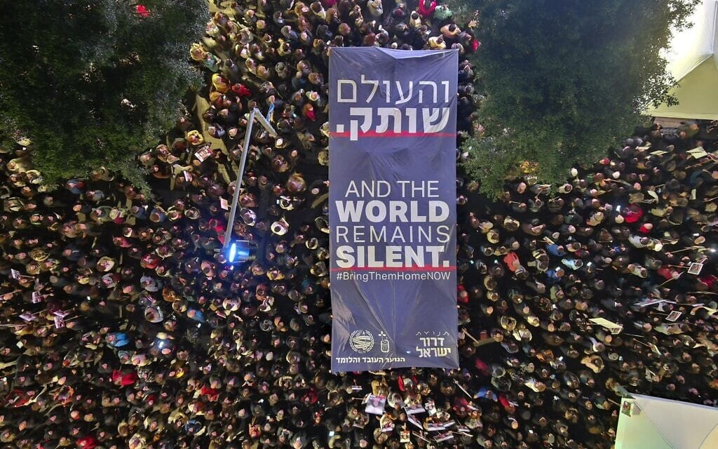 שלט "והעולם שותק" שנשאו חניכי הנוער העובד והלומד בעצרת למען החטופים. 13 בינואר 2024 (צילום: אביב אטלס)