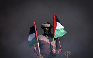 צעיר פלסטיני מחזיק דגלי פלסטין ליד גדר הגבול בעזה, 3 ביולי 2023 (צילום: MAHMUD HAMS / AFP)