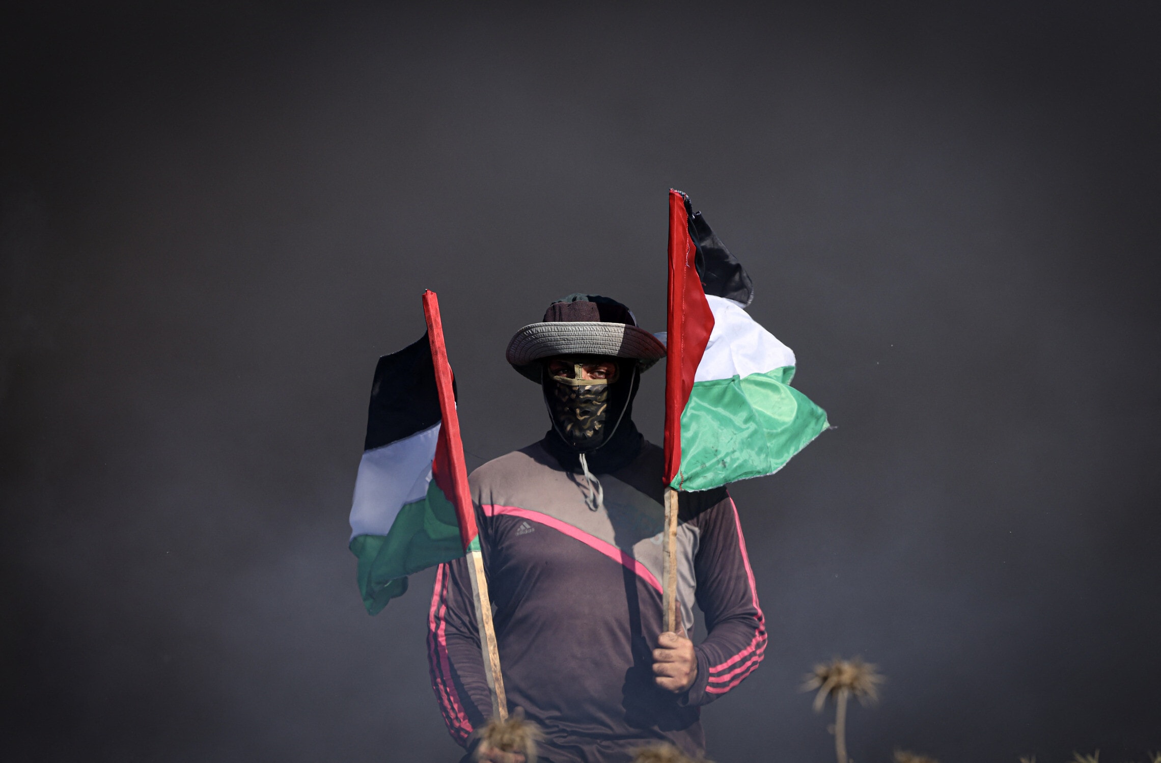 צעיר פלסטיני מחזיק דגלי פלסטין ליד גדר הגבול בעזה, 3 ביולי 2023 (צילום: MAHMUD HAMS / AFP)