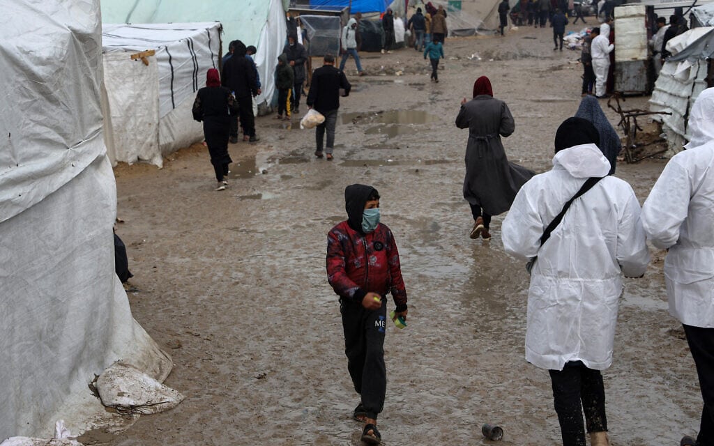 פלסטינים הולכים בגשם במחנה מאולתר ברפיח שבדרום רצועת עזה, 2 בפברואר 2024 (צילום: Mohammed ABED / AFP)