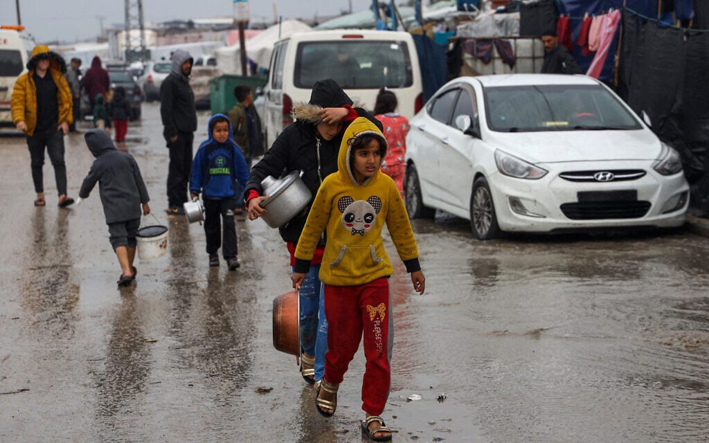 פלסטינים הולכים בשלולית במזג אוויר גשום כדי לקבל מנות מזון במחנה אוהלים מאולתר ברפיח שבדרום רצועת עזה, 2 בפברואר 2024 (צילום: Mohammed ABED / AFP)